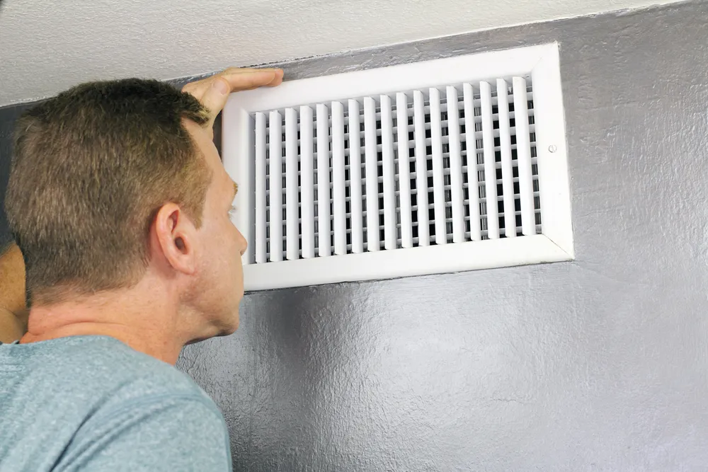 Man inspecting wall air vent grille