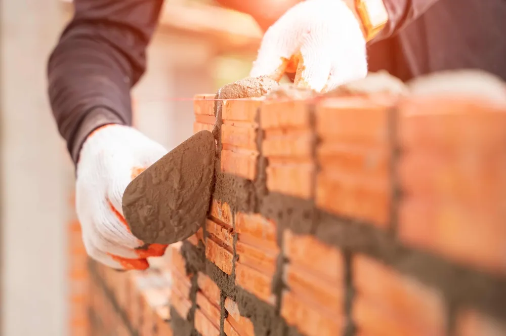 Bricklayer applying mortar to brick wall with trowel
