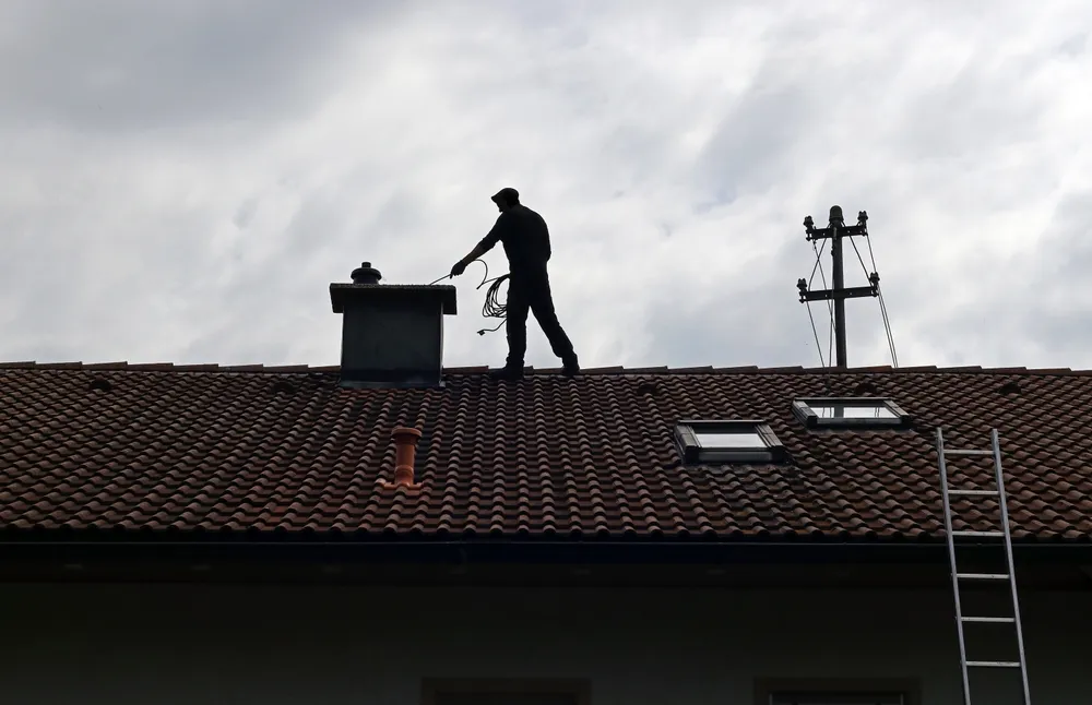 Roofer cleaning chimney on tiled house roof