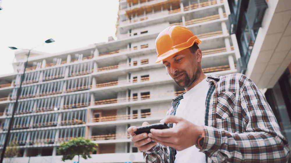 Construction worker in hard hat using smartphone on site