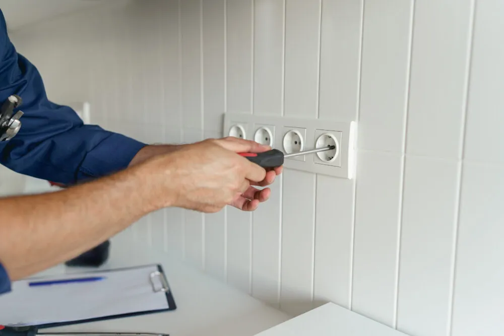 Electrician repairing wall power outlet with screwdriver