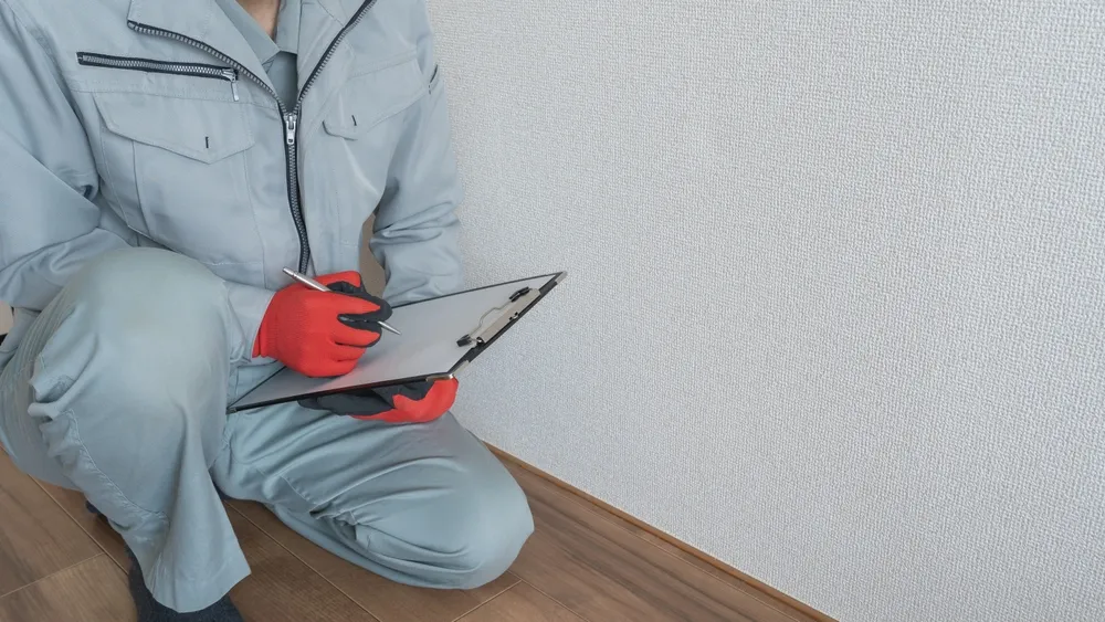 Tradesperson inspecting wall with clipboard and gloves