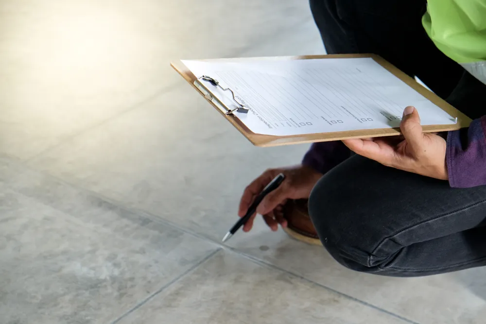 Inspector checking floor tiles with clipboard and pen