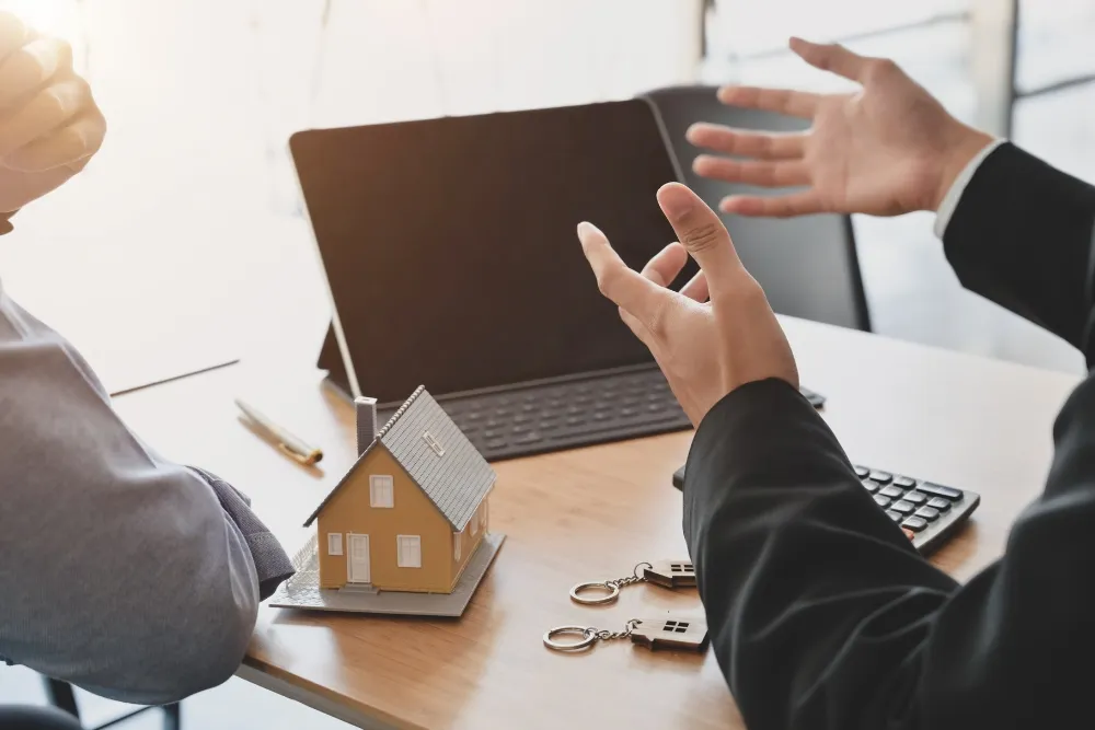 Open hands and a house miniature and tablet on desk