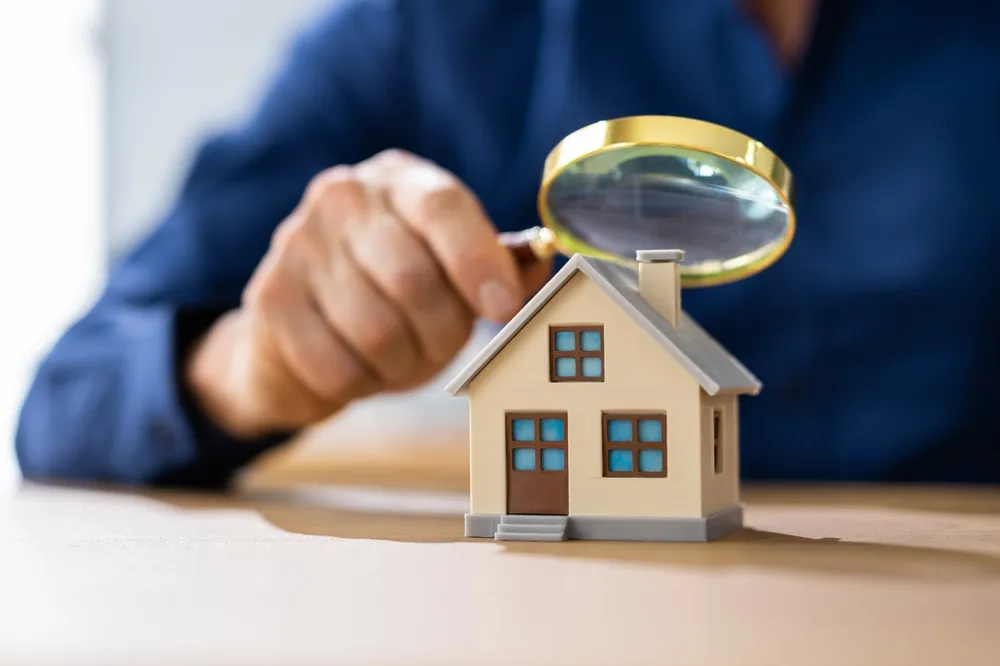 Magnifying glass inspecting model house for property assessment