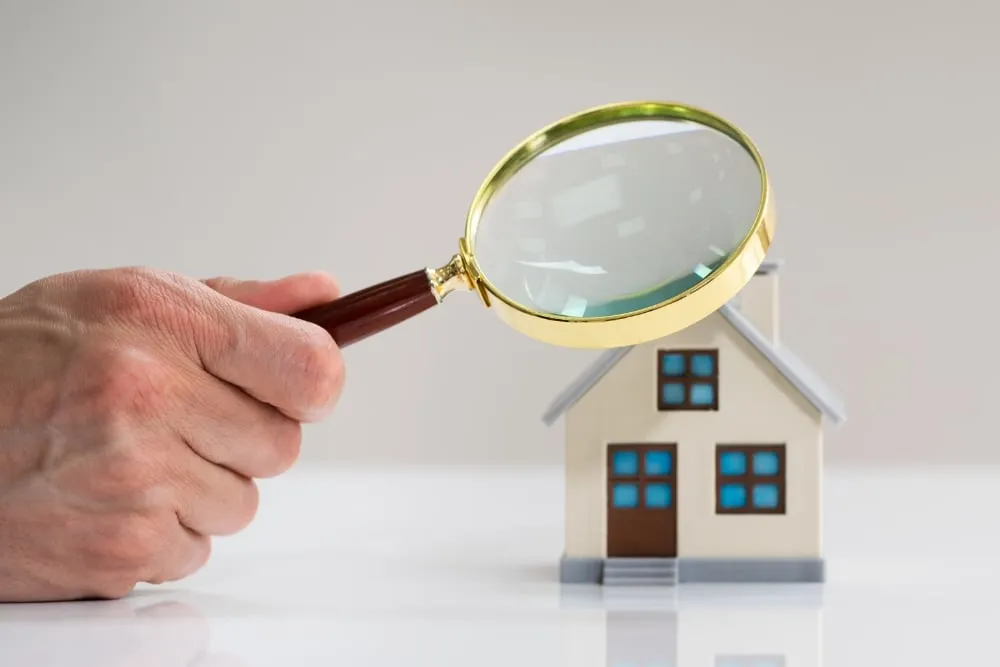 Hand holding magnifying glass over model house