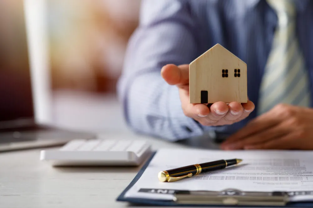 Person holding wooden house model over paperwork