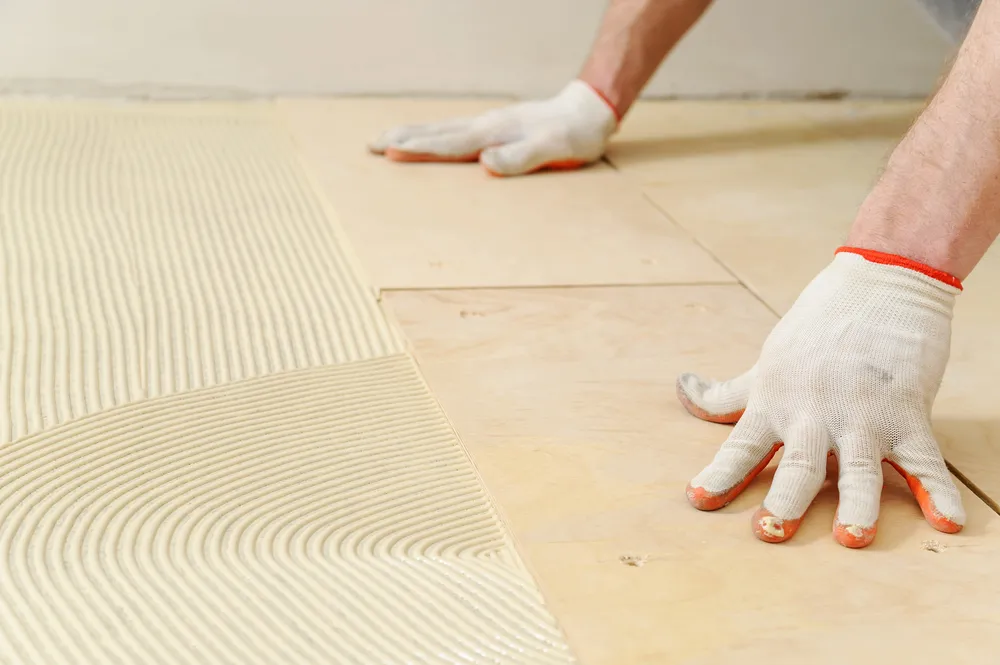 Gloved hands laying floor tiles with adhesive