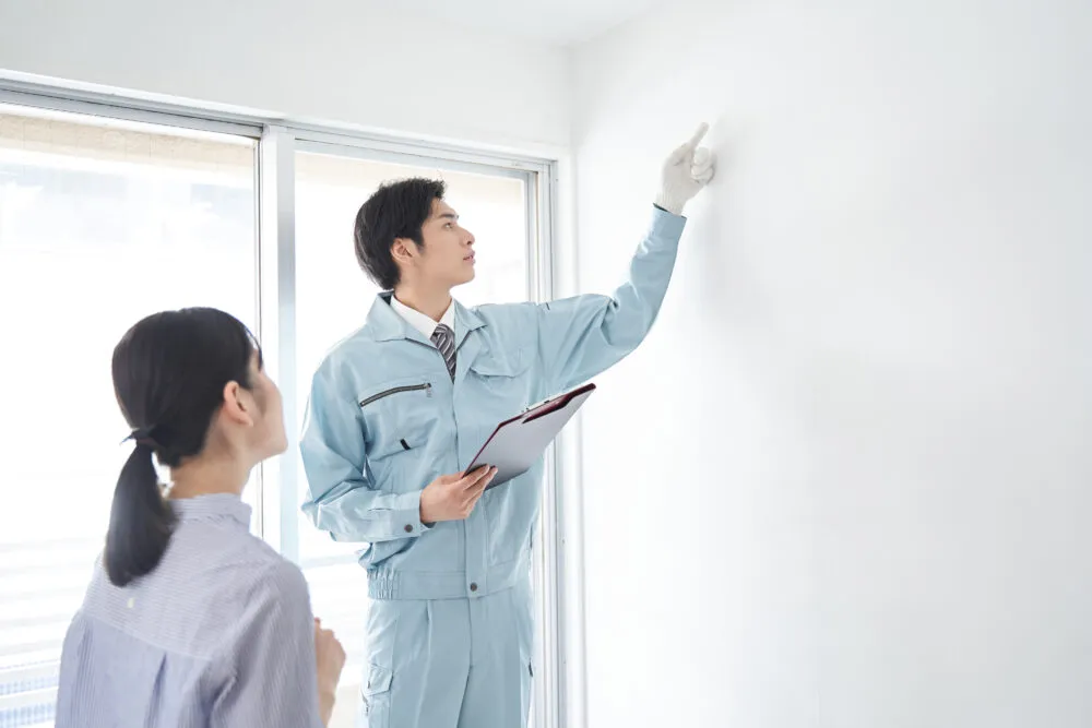Tradesman inspecting interior wall with homeowner watching