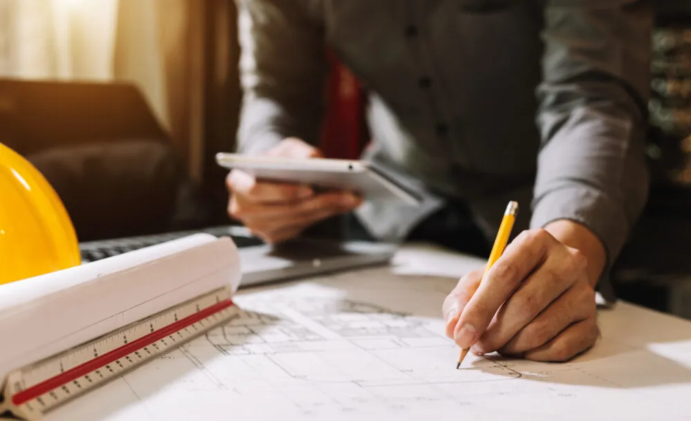 Architect reviewing building plans with tablet and hard hat