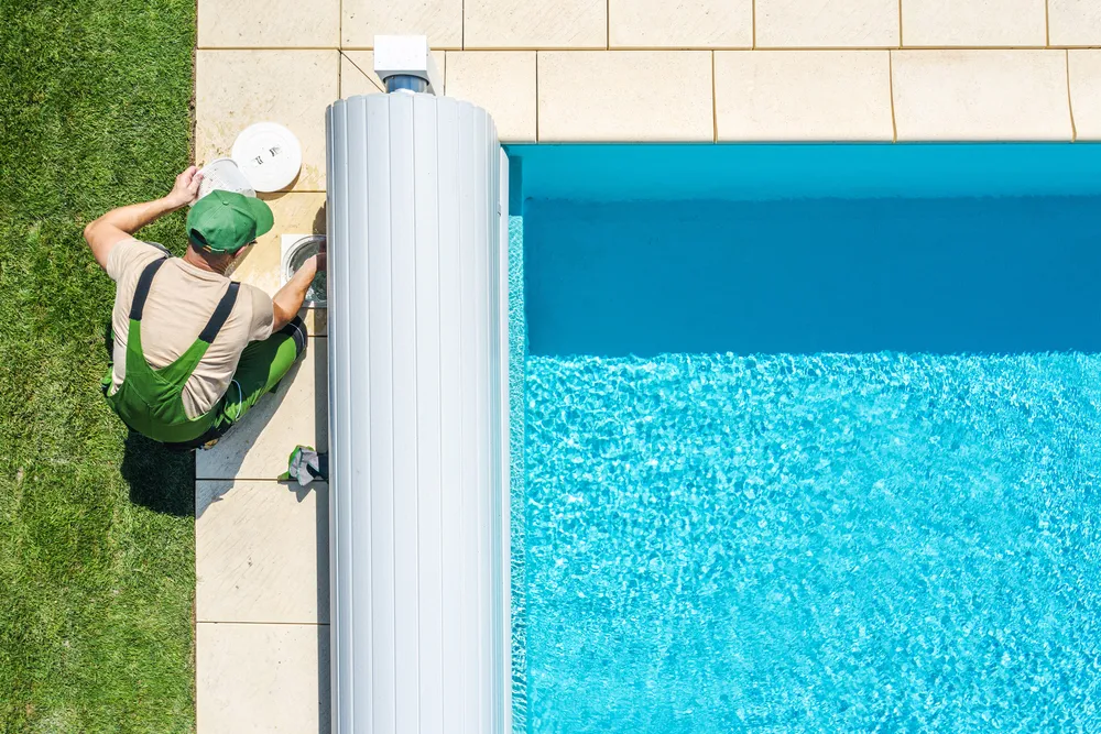 Pool technician servicing backyard swimming pool skimmer