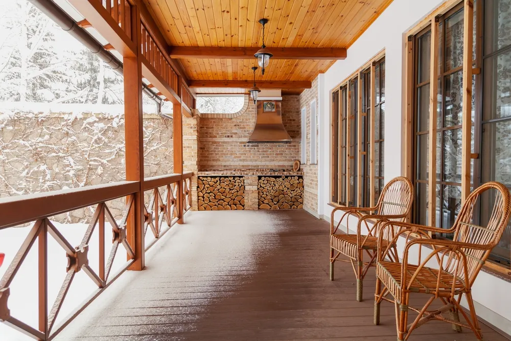 Covered wooden veranda with wicker chairs and barbecue